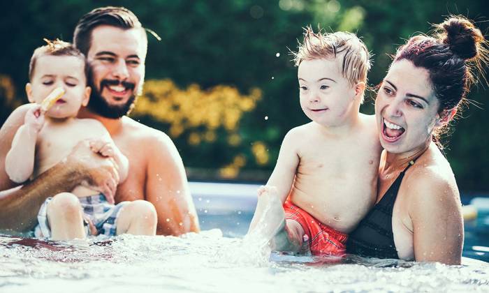 Little boy with Down syndrome eating popsicle in the swimming pool with his family