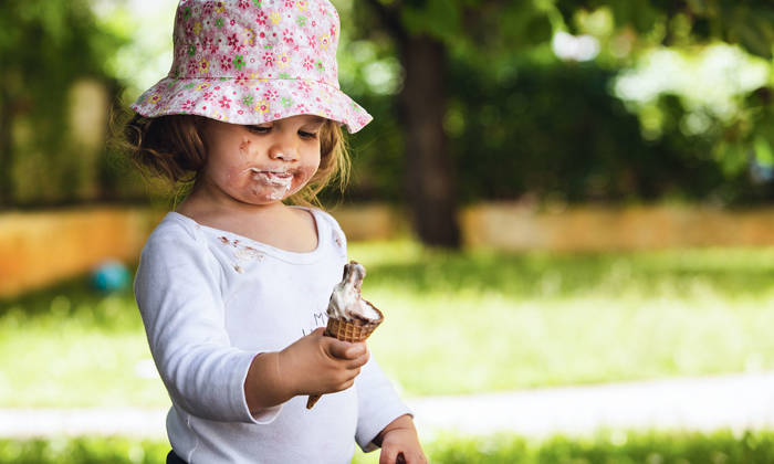 Girl standing in park eating ice cream that is melting.