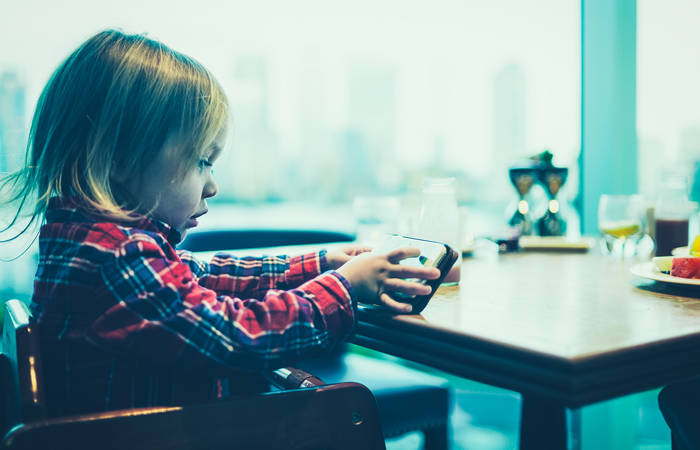 A toddler is using a smartphone at the breakfast table